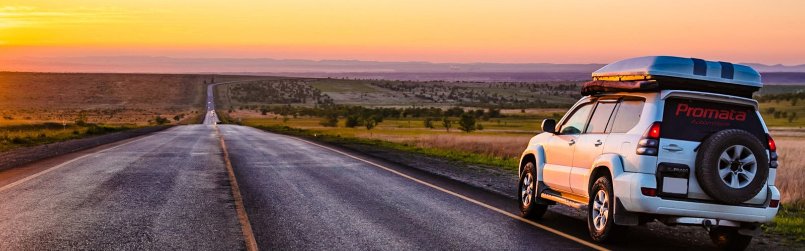 Promata car with roof rack and spare tire on a road at sunset